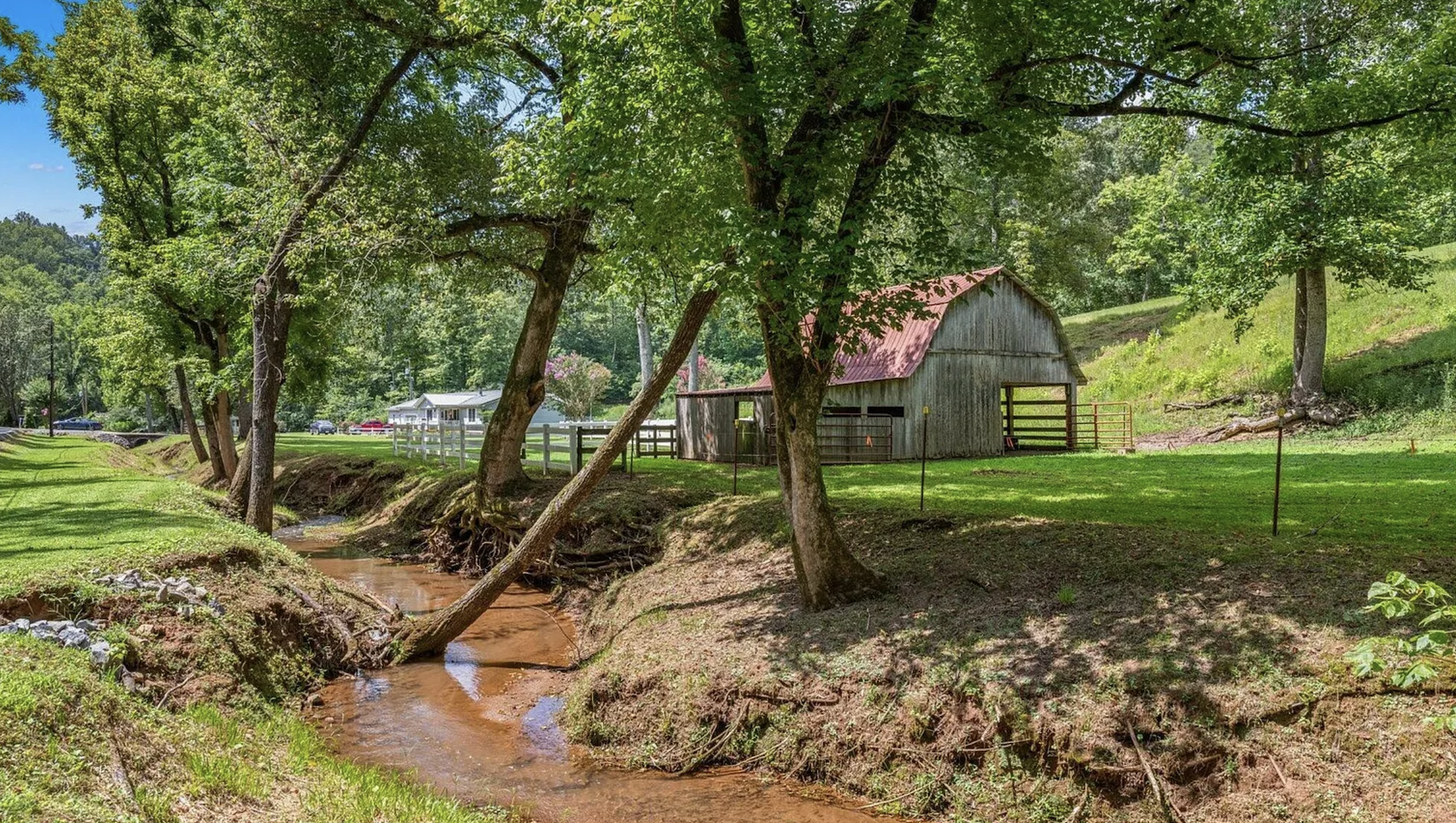 Property view with pond/waterfall feature, white fence, and gravel driveway